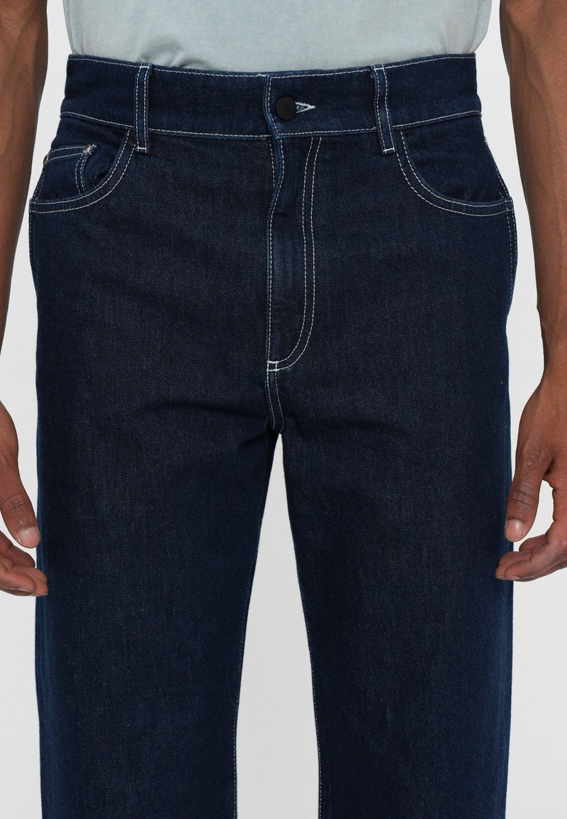 Jeans in denim blu scuro con cuciture bianche a contrasto, chiusura a bottone, tasche laterali e gamba dritta.