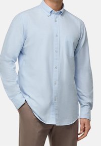 Ljusblå skjorta i bomullsblandning med knappar, som har en ficka, krage och långärmar, uppvisad tillsammans med beige byxor.