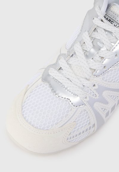 Adidași albi din material de plasă, cu accente argintii, vârf texturat din suede și detalii complicate pe laturi și limbă. Sforile sunt albe.
