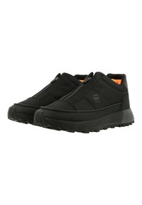 Svarta slip-on skor med en strukturerad ovandel, som har en blixtlåsstängning och en tjock, robust yttersula för bra grepp. Ljusa orange detaljer på insidan.