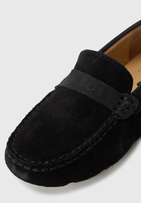 Svarta mockaloafers med rund tå, med ett gummiband och präglad logotyp på framsidan, slät innerv lining och sömdetaljer.