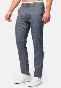 Chinos grises para hombre con una sutil textura tejida, ajuste entallado, cremallera y cierre de botón. Combinados con zapatillas blancas, que presentan líneas limpias.