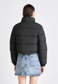 Svart pufferjakke med høy krage, med horisontale seksjoner. Kombinert med en lys blå denimskjørt med broderte lapper på lommene.