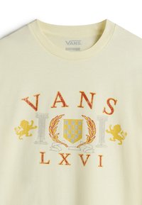 Lichtgele katoenen t-shirt met een rood en gouden "VANS" logo, decoratieve leeuw graphics en kolom illustraties. Ronde halslijn.