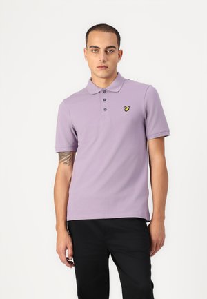 Lila Poloshirt mit einem Kragen, drei Knöpfen und einem gelben Logodetail auf der Brust. Kurze Ärmel und eine glatte Textur.