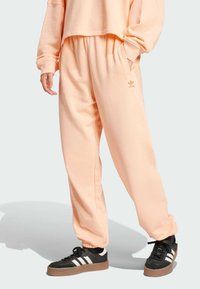 Lososové teplákové nohavice vyrobené z mäkkého materiálu, s voľným strihom, bočnými vreckami a logom Adidas v svetlejšej farbe.