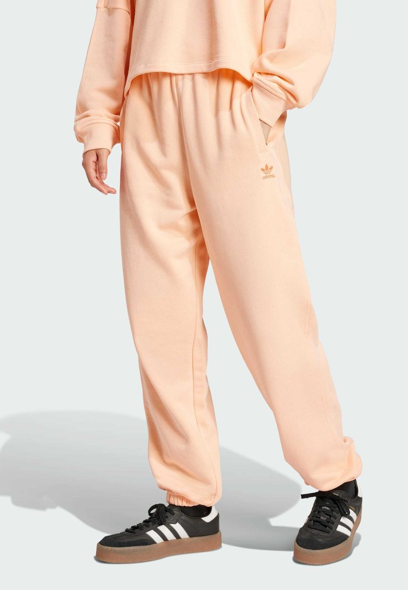 Lososové teplákové nohavice vyrobené z mäkkého materiálu, s voľným strihom, bočnými vreckami a logom Adidas v svetlejšej farbe.