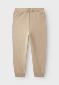 Beige Jogginghose mit elastischem Bund und gerippten Bündchen, flach auf einem hellen Hintergrund liegend.