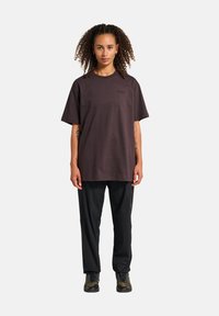 Przesadna ciemno-brązowa koszulka bawełniana z okrągłym dekoltem i krótkimi rękawami, z delikatnym logo na piersi. W połączeniu z czarnymi spodniami i trampkami.