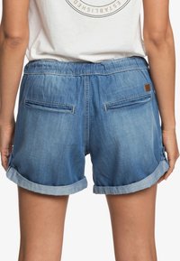 Short en denim bleu clair, avec une ceinture élastique, des revers roulés et deux poches arrière. Tissu texturé à l'apparence lisse.