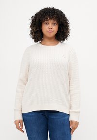 Kremfarget strikket genser med et teksturert mønster, ribbestrikkede mansjetter og rund hals, sammen med denimjeans.