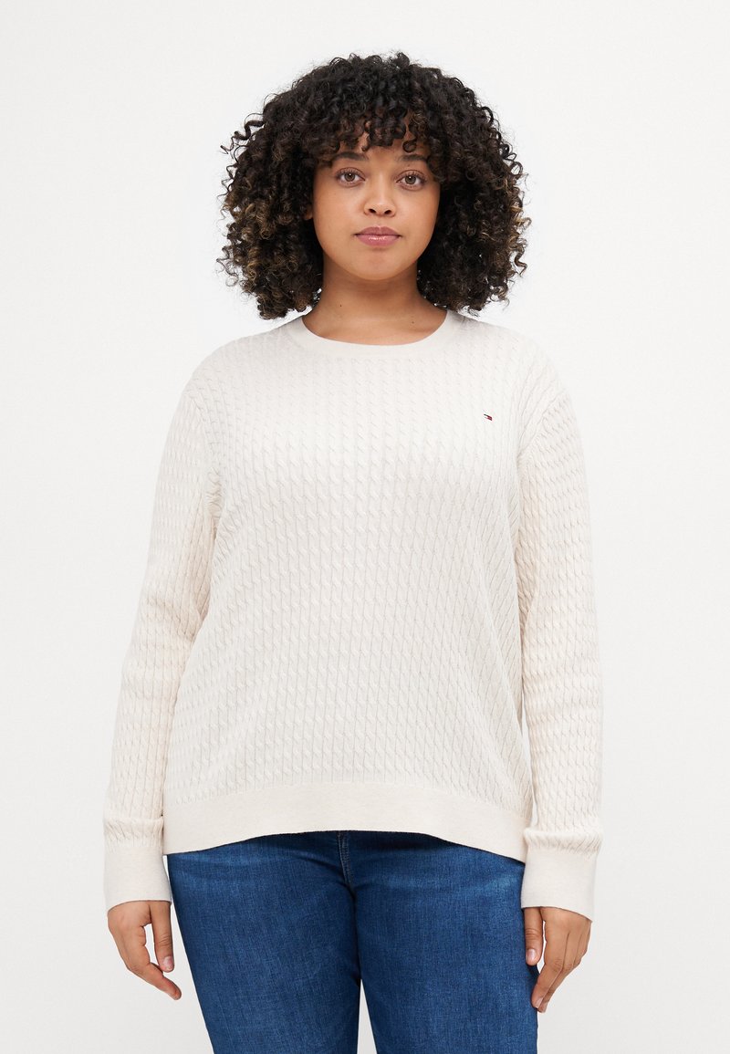 Kremfarget strikket genser med et teksturert mønster, ribbestrikkede mansjetter og rund hals, sammen med denimjeans.