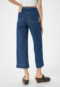 Korkeavyötäröiset siniset farkut suoran lahjetta, kahdella takataskulla ja raidoitetulla helmalla. Kankaan pinnassa on tekstuuri.