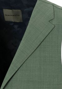 Grüne Blazer mit scharfen Revers, strukturierter Stoff und einem dunklen gemusterten Innenfutter. Mit einem Etikett mit der Aufschrift "BENVENUTO".