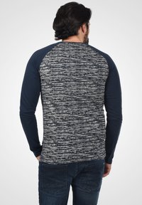 Langermet skjorte med en teksturert grå og marineblå stripet design, med kontrastfargede marineblå ermer og rund hals. Stoffet ser mykt ut.