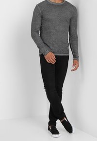 Harmaa pitkähihainen T-paita vartalonmyötäisessä mallissa, yhdistettynä mustiin slim fit -farkkuihin ja mustiin liukuviin kenkiin. Sileä tekstuuri, ei näkyviä kuvioita.