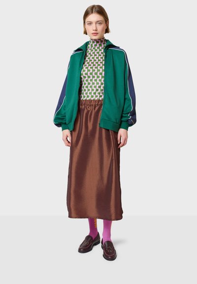 Zelena i mornarsko plava zip-up jakna preko uzorkovane rolke, smeđa satenska suknja, ružičaste čarape, smeđi mokasini s vezom.