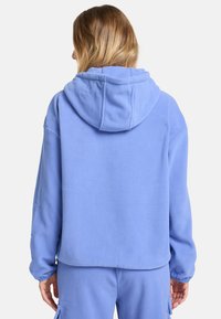 Haut à capuche en polaire bleue avec une grande capuche, coupe décontractée et texture douce. Doté de manches à revers et d'une taille qui tombe au niveau des hanches.