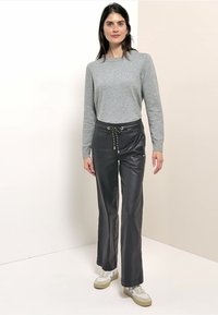 Haut gris à manches longues avec un col rond, associé à un pantalon noir brillant à coupe ample, équipé d'un cordon de serrage et de poches latérales. Baskets blanches et beiges.