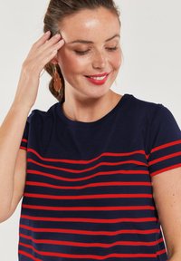 Granatowy T-shirt z poziomymi czerwonymi paskami, krótki rękaw i okrągły dekolt. Gładka bawełniana tkanina w luźnym kroju.