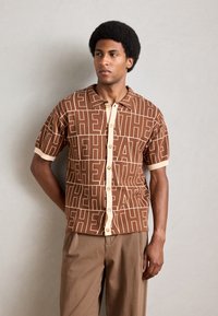 Short-sleeve brown patterned shirt with oversized text design. Cream accents on collar and cuffs. Buttons down the front.