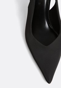 Crne štikle s šiljastim vrhom izrađene od glatkog sintetičkog materijala. Odlikuju se elegantnim dizajnom s izrezima sa strane za dodatne detalje.