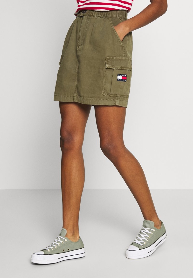 Shorts cargo vert olive avec une ceinture élastique, des poches latérales et un patch Tommy Jeans. Associés à des baskets en toile vert clair.