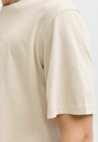 Beiges T-Shirt aus Baumwolle mit kurzen Ärmeln und rundem Ausschnitt. Verfügt über einen dezenten Markenaufdruck und eine einfarbige Struktur mit sichtbaren Nahtdetails.