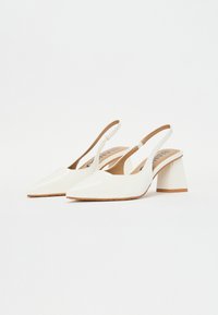 White patent leather slingback heels with a pointed toe and chunky block heel. Interior features a brown cushioning detail.