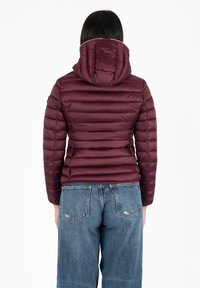 Bordeaux pufferjack met horizontaal gestikt patroon en aangehechte capuchon. Gecombineerd met blauwe jeans, wat een casual, gelaagd uiterlijk oplevert.