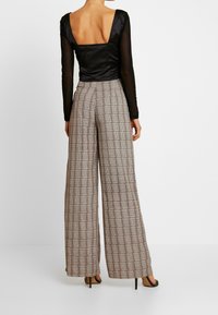 Černý saténový top s dlouhými rukávy a čtvercovým výstřihem na zádech, v kombinaci s béžovými kostkovanými širokými kalhotami a černými lodičkami na vysokém podpatku.