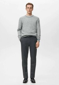 Maglione grigio testurizzato abbinato a pantaloni sartoriali color grigio scuro e scarpe in pelle nera. L'outfit presenta un collo a girocollo e un design a gamba dritta.