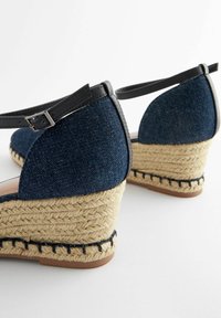Sandali con zeppa in denim con cinturini in pelle nera, tacco avvolto in juta e finitura testurizzata. Presentano una cinghia alla caviglia con dettaglio in fibbia metallica.