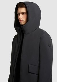 Schwarze Kapuzenjacke mit glatter Textur, durchgehendem Frontreißverschluss und einem Logo-Patch am linken Ärmel. Sie verfügt über zwei Fronttaschen.
