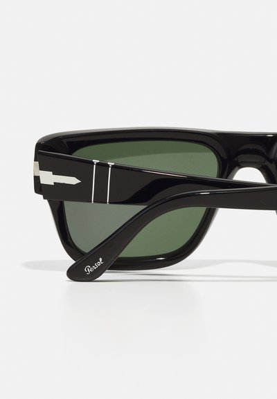 Fekete napszemüveg zöld lencsékkel. Ezüst részletekkel a kereten és a szárakon, elegáns kialakítással és lekerekített formával. Logó a szárakon.