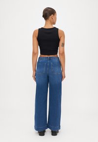 Black cropped tank top paired with wide-leg blue denim pants, featuring two back pockets and a cuffed hem. Smooth texture and casual fit.