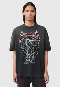 Zwart oversized T-shirt met een grafisch ontwerp van een schedel omwikkeld met slangen, met rode letters bovenaan. Katoenen materiaal, korte mouwen.