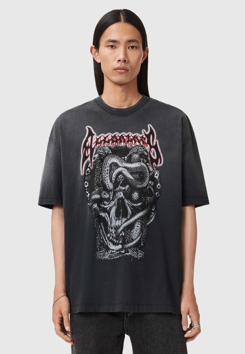 Zwart oversized T-shirt met een grafisch ontwerp van een schedel omwikkeld met slangen, met rode letters bovenaan. Katoenen materiaal, korte mouwen.