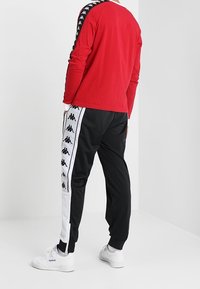 Rode langemanige shirt met zwarte patroonaccenten op de mouwen, gecombineerd met zwarte joggers met witte zijkanten en logodetails.