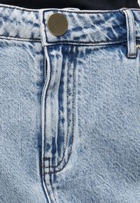 Τζιν ελαφρού μπλε όξινου πλυσίματος που δείχνει τη μέση της μέσης, μεταλλικό κουμπί, θηλιά ζώνης και μέρος της μπροστινής τσέπης με ορατές ραφές.