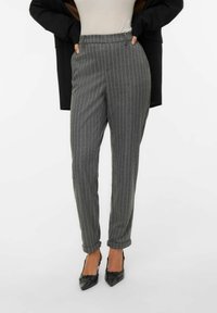 Szare spodnie w prążki o dopasowanym kroju, z wysokim stanem i podwiniętymi mankietami, zestawione z czarnymi szpilkami w szpic.