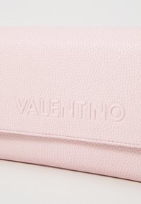 Roosa nahast käekott, millel on tekstureeritud pind ja reljeefne "VALENTINO" logo. Disain on puhas ja struktureeritud, sleek sulgemisega.
