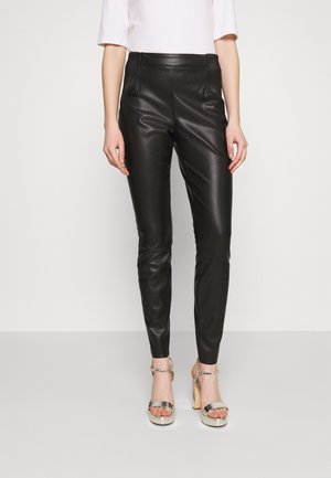 Pantalons en faux cuir noir au design ajusté, dotés de poches avant et de détails côtelés le long de la taille. Associés à des sandales à talons argentées.