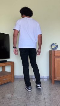Valge lühikeste varrukate jaotust, mustad kitsad püksid ja mustad Nike tossud. Taustal on puidust televiisori alus ja dekoratiivne ese.
