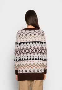 Pull en tricot avec un motif de dessins géométriques en blanc, marron et tons terre, avec un col rond et des manches longues.