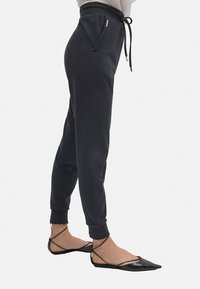 Pantalones de chándal negros con cintura elástica y cordón, que presentan bolsillos laterales y puños ajustados. Combinados con unas bailarinas negras con tiras.