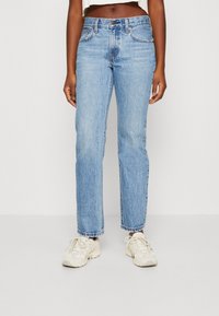 Jeans de mezclilla azul claro con un diseño de pierna recta, cintura de media altura y dobladillo deshilachado. Combinados con zapatillas beige.