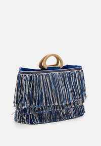  fransad handväska med ett dubbelt ringhandtag i trä. Tillverkad av blå och beige trådar, med lager av fransdetaljer och en strukturerad design.