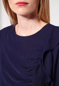 Marinblå topp med mjukt tyg, rund halsringning och samlad detalj på sidan. Slät textur med avslappnad passform.
