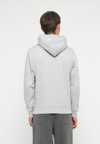 Sudadera gris con capucha, con una textura suave y puños acanalados. La parte trasera presenta un diseño simple con un corte relajado.